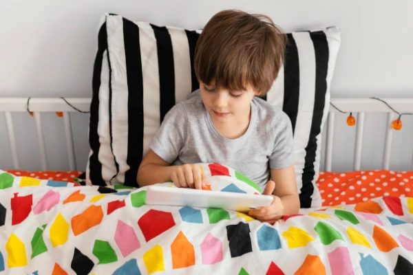 Ein Junge spielt mit einem Tablet in einem bunten Kinderbett