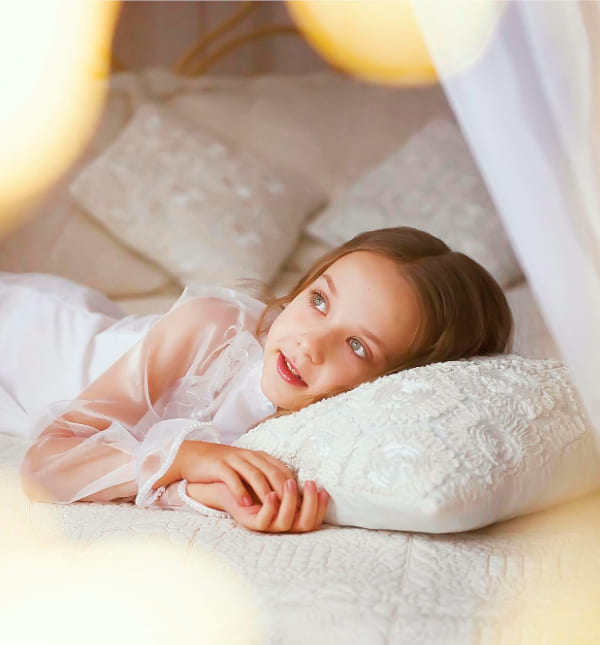 Kleines Mädchen im gemütlichen Kinderbett blickt verträumt aus dem Fenster